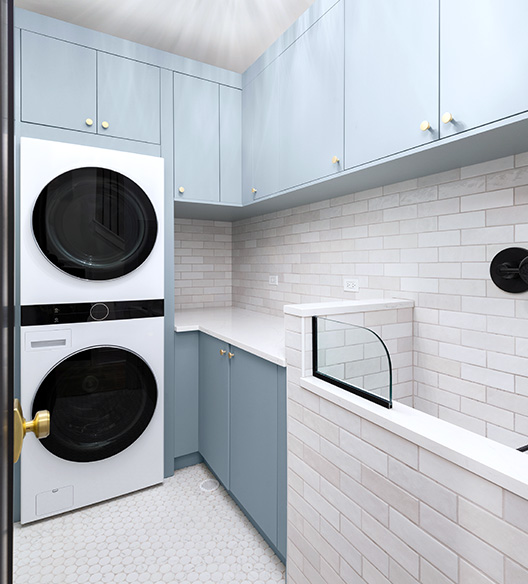 A modern luxurious laundry room with powder blue cabinets with a white washer and dryer